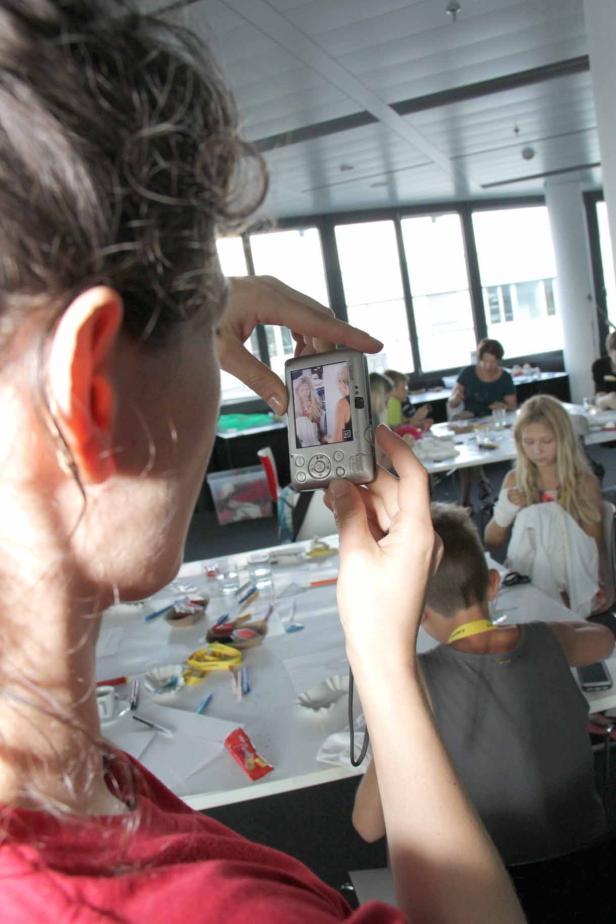 Eine Frau fotografiert mit einer Digitalkamera ein Bild von zwei Frauen.