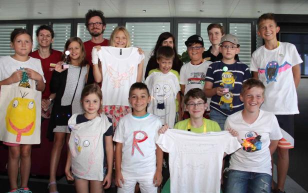 Eine Gruppe von Kindern und Erwachsenen posiert mit selbstgestalteten T-Shirts und Taschen.