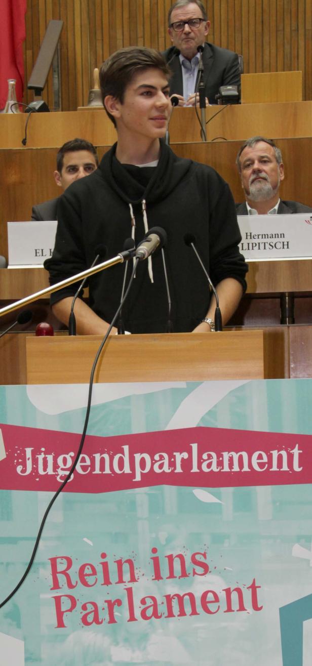 Ein junger Mann spricht im Jugendparlament vor mehreren Mikrofonen.