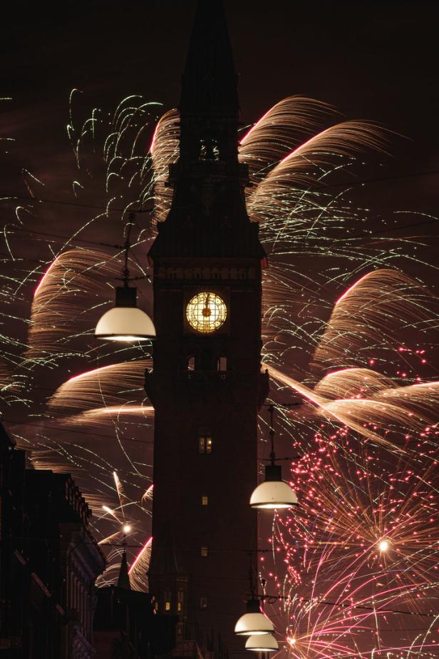 Feuerwerk erhellt den Nachthimmel über einem dunklen Turm mit einer beleuchteten Uhr.