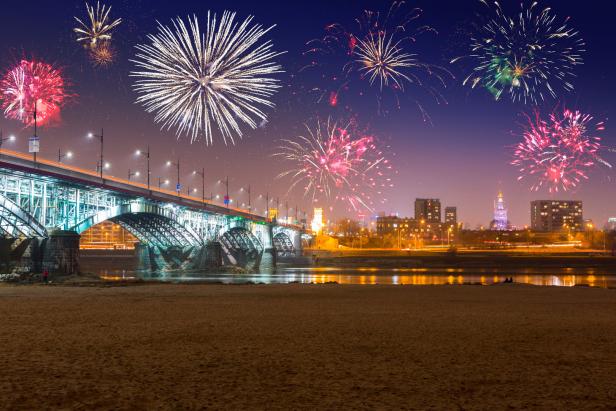 Feuerwerk erhellt den Himmel über einer Stadt mit einer Brücke und einem Fluss.