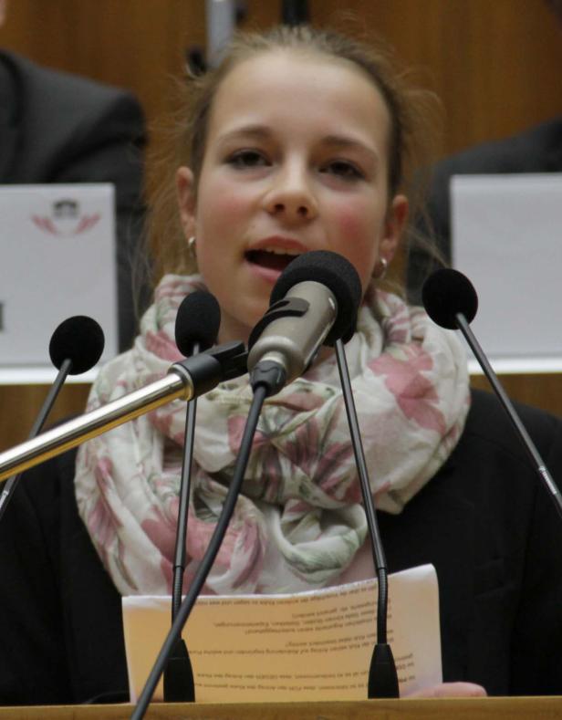 Ein junges Mädchen spricht bei einer Veranstaltung in mehrere Mikrofone.