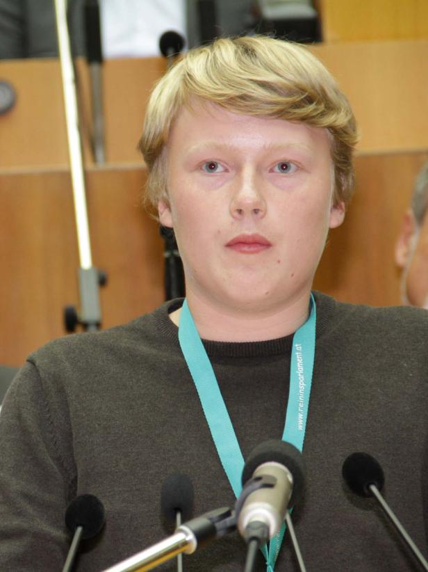 Ein junger Mann mit blonden Haaren steht vor mehreren Mikrofonen.