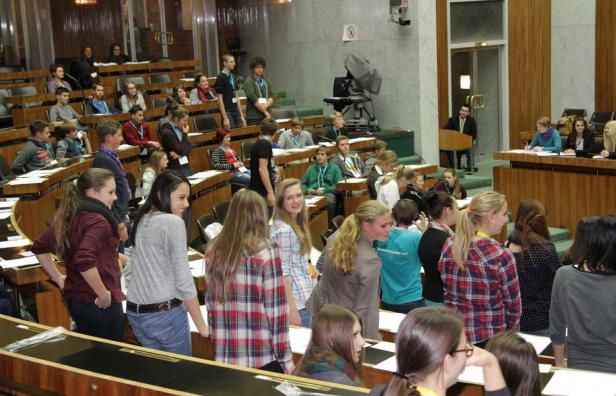 Eine Gruppe junger Leute sitzt in einem großen Saal mit holzvertäfelten Wänden.