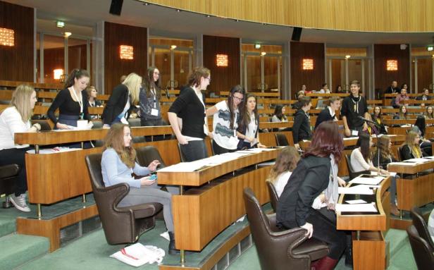 Jugendliche sitzen in einem holzvertäfelten Saal mit Pulten.