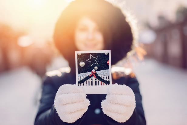 Eine Frau mit Handschuhen hält ein Foto von einem Weihnachtsbaum.