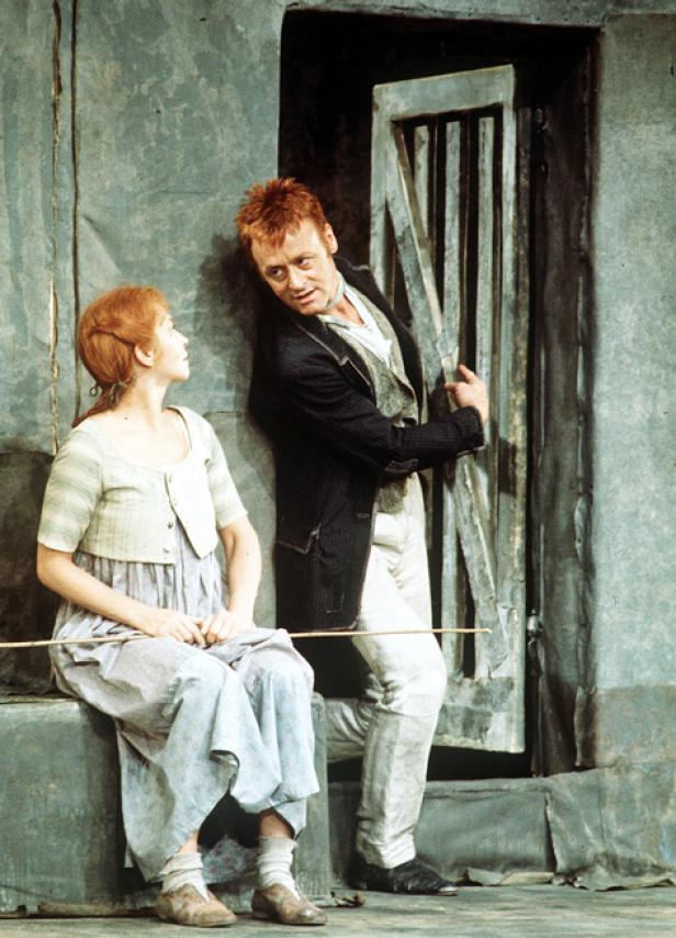 Eine Frau sitzt, während ein Mann an eine Tür gelehnt zu ihr aufschaut.