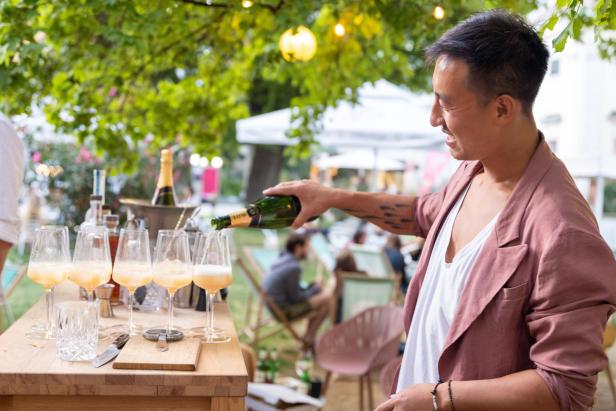 Ein Mann schenkt Sekt in Gläser auf einer Gartenparty ein.
