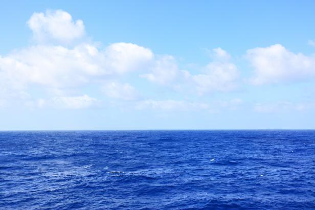 Ein ruhiger, blauer Ozean unter einem hellblauen Himmel mit weißen Wolken.