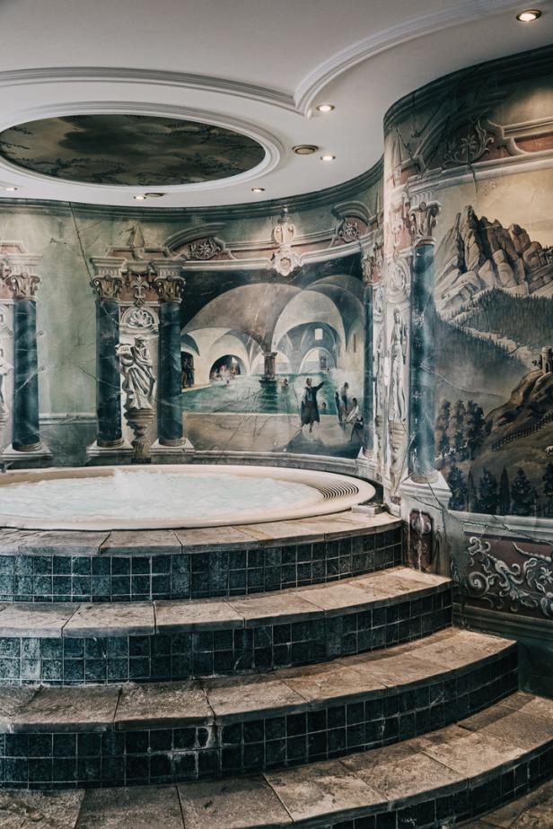 Ein Whirlpool ist von einer bemalten Wand mit Säulen und einer Badeszene umgeben.