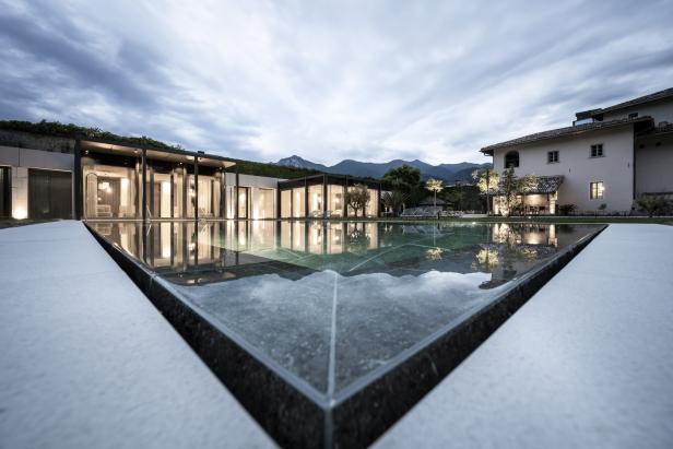 Ein Schwimmbad spiegelt moderne Architektur vor einer Bergkulisse wider.