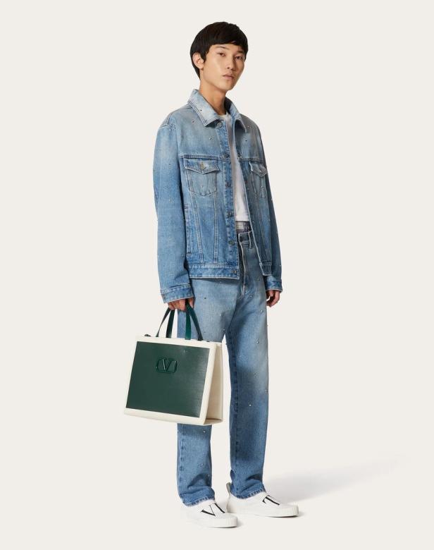 Ein Mann in Jeansjacke und -hose hält eine Valentino-Tasche.
