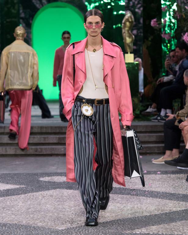 Ein Model in einem rosa Mantel und gestreiften Hosen auf einem Laufsteg.