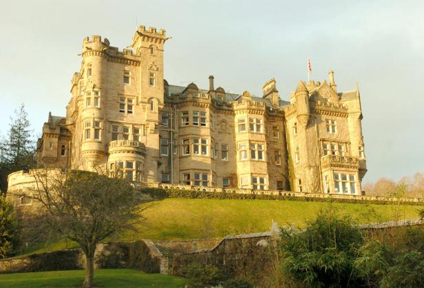 Ein großes Schloss mit vielen Fenstern steht auf einem grünen Hügel.