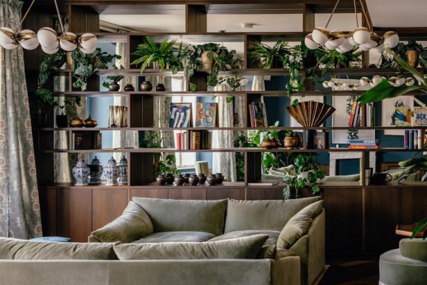 Ein Wohnzimmer mit einem Bücherregal voller Pflanzen, Büchern und dekorativen Objekten über einem grünen Sofa.
