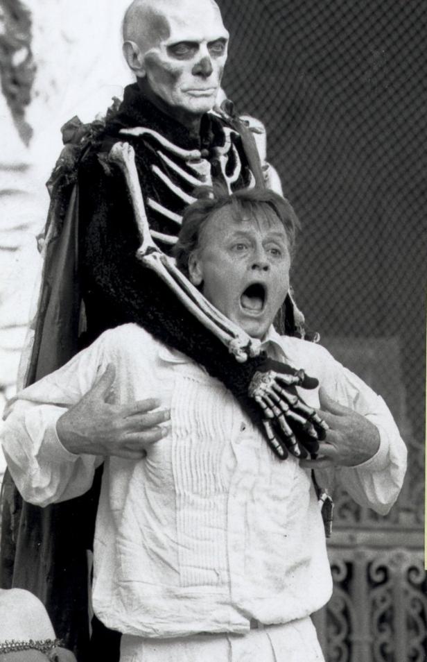 Ein Mann in weißem Hemd wird von einer als Skelett verkleideten Person erschreckt.