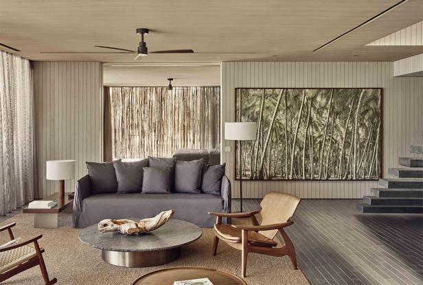 Ein Wohnzimmer mit einem grauen Sofa, einem Holztisch und einem großen Bild von Palmen.