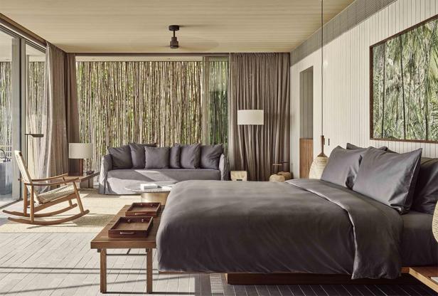 Innenansicht einer Villa im Patina Maldives mit Bett, Sofa und Schaukelstuhl.