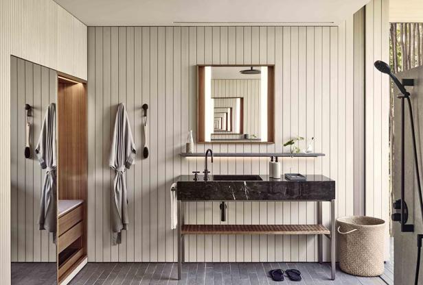 Ein Badezimmer mit Marmorwaschtisch, Spiegel und Bademänteln an der Wand.