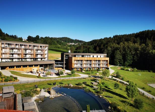 Ein modernes Hotelresort mit einem Teich und viel Grünfläche an einem sonnigen Tag.