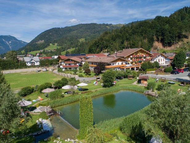 Luftaufnahme eines malerischen Dorfes mit einem Schwimmteich im Vordergrund.