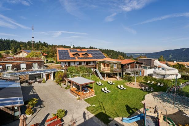 Ein Blick auf ein Resort mit Spielplatz, Liegewiese und Wasserrutsche vor bewaldeten Hügeln.