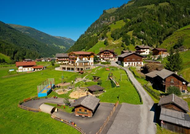 Ein Feriendorf mit Spielplatz liegt eingebettet in eine grüne Berglandschaft.