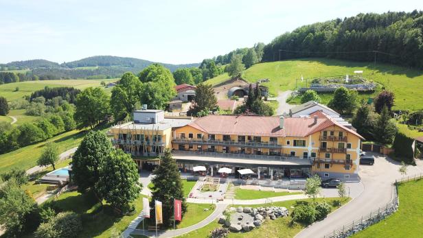 Ein großes Hotel liegt in einer grünen Landschaft mit Hügeln und Bäumen.
