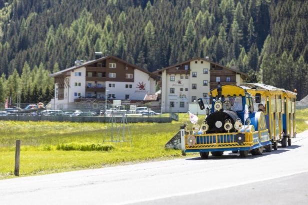Ein Touristenzug fährt auf einer Straße vor einer bewaldeten Landschaft.
