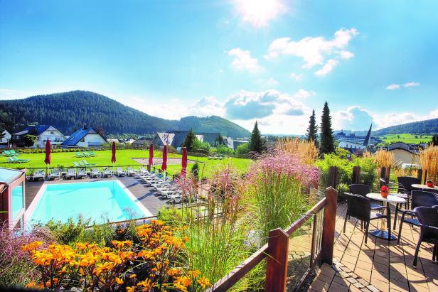 Ein Schwimmbad mit Liegestühlen vor einer grünen Landschaft mit Häusern und Bergen.