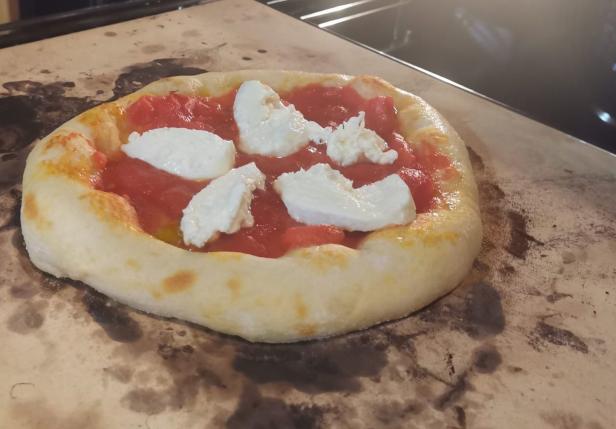 Eine Pizza mit Tomatensauce und Mozzarella auf einem Pizzastein.