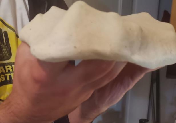 Eine Person hält einen rohen Pizzateig in der Hand.