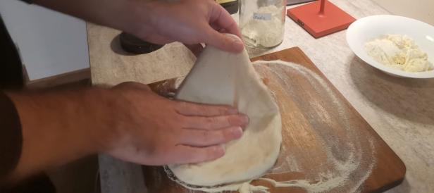 Eine Person formt einen Pizzateig auf einem Holzbrett.