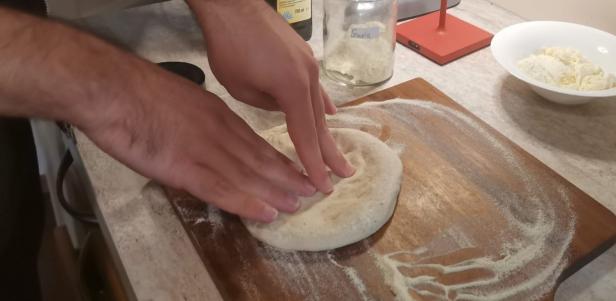 Eine Person formt einen Pizzateig auf einem bemehlten Holzbrett.