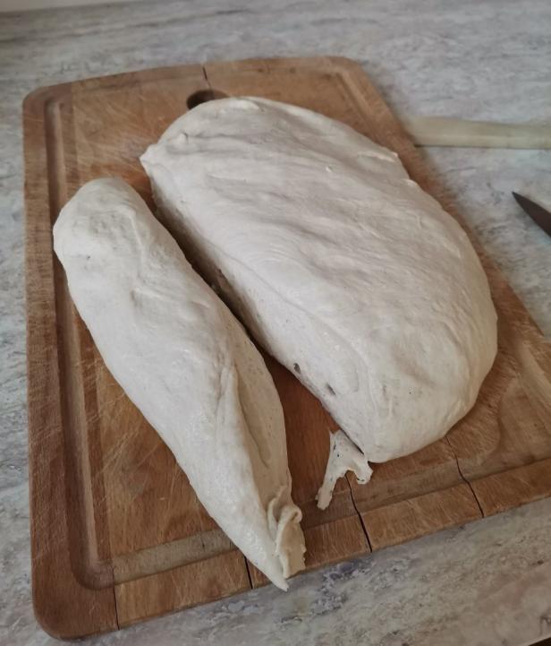 Ein Stück roher Teig liegt auf einem Holzbrett.