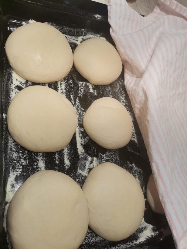 Rohe Teiglinge liegen auf einem Backblech unter einem Küchentuch.
