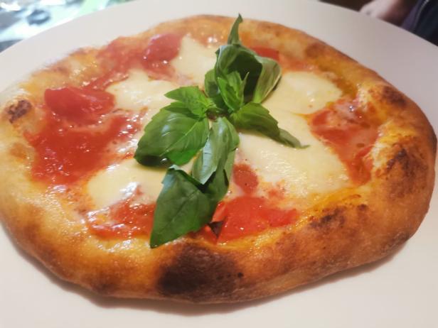 Eine Pizza Margherita mit Tomaten und Basilikum auf einem Teller.