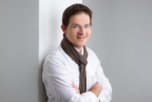 Ein Mann mit Brille und Schal lehnt an einer Wand.