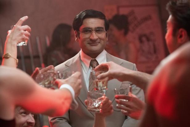 Kumail Nanjiani in Anzug wird von Leuten mit Gläsern umringt.