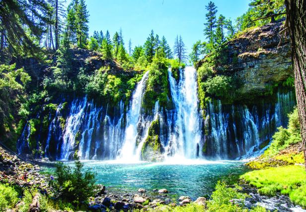 Ein Wasserfall ergießt sich in einen türkisfarbenen See, umgeben von Bäumen und Felsen.