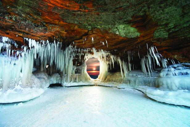 Eiszapfen hängen von der Decke einer Höhle, durch deren Öffnung die Sonne scheint.