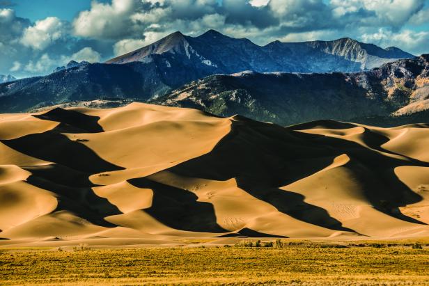 Sanddünen erstrecken sich vor einer Bergkette unter einem bewölkten Himmel.