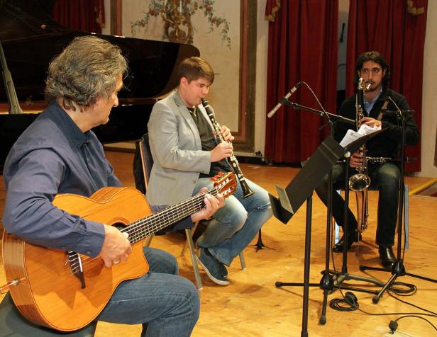 Drei Musiker spielen Gitarre, Klarinette und Saxophon auf einer Bühne.