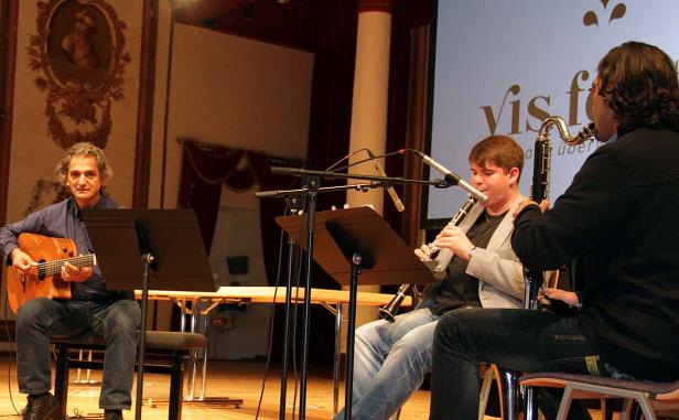 Drei Musiker spielen Gitarre und Klarinette auf einer Bühne.