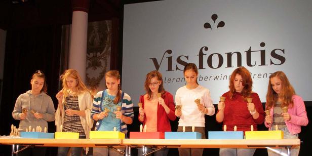 Eine Gruppe junger Frauen spielt auf einem Tisch mit Handglocken vor einem Publikum.