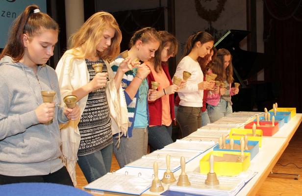 Eine Gruppe junger Frauen spielt auf Handglocken vor Notenblättern.