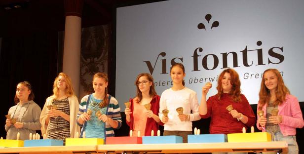 Eine Gruppe junger Frauen spielt auf einem Tisch mit Handglocken vor einem Publikum.