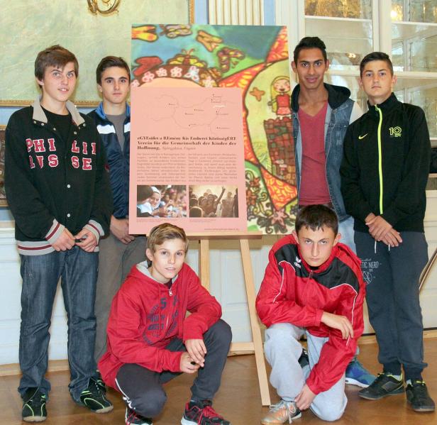 Eine Gruppe von Jungen steht vor einem Plakat des Vereins „Remény Kis Emberei KözösségÉRT“.