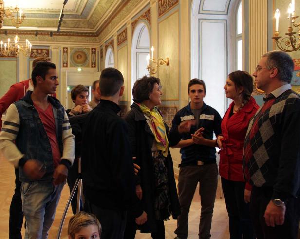 Eine Gruppe von Menschen steht in einem reich verzierten Raum und unterhält sich.