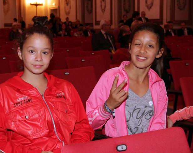 Zwei junge Mädchen sitzen in einem Theatersaal und lächeln in die Kamera.